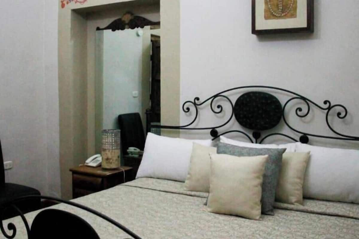A bedroom with a bed, pillows, a nightstand, a phone, and a mirror.