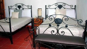 Two metal beds with headboards, a wooden nightstand, and a red tiled floor.