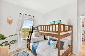 Ein Etagenbett mit einer Leiter, weiße Bettwäsche und dekorative Kissen. Ein Fenster mit Vorhängen bietet einen Blick ins Freie.