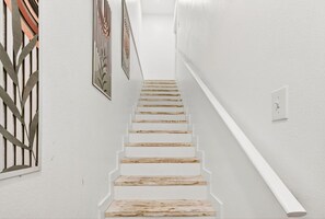 Eine Treppe mit Holzdielen, die nach oben führt, weiße Wände und ein schmiedeeisernes Gitter links.