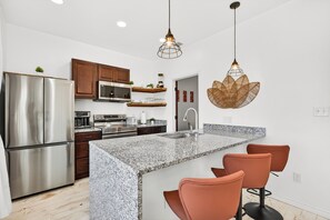 Een moderne keuken met granieten aanrechtbladen, roestvrijstalen apparatuur en een centraal eiland met barkrukken.