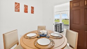 A dining area with a round table set for four, chairs, and a view of a balcony. - Lux 2BR-2BA: Boardwalk + 3rd Floor Deck (Port Aransas)