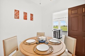 A dining area with a round table set for four, chairs, and a view of a balcony. - Lux 2BR-2BA: Boardwalk + 3rd Floor Deck (Port Aransas)
