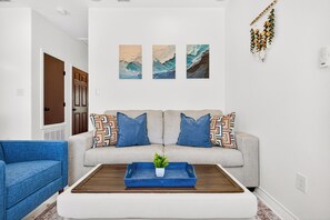 Een woonkamer met een bank, blauwe fauteuil, salontafel en wanddecoratie.