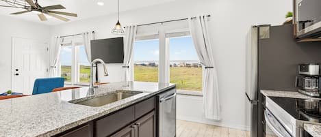 Una cocina moderna con encimera de granito, electrodomésticos de acero inoxidable y vistas al exterior.