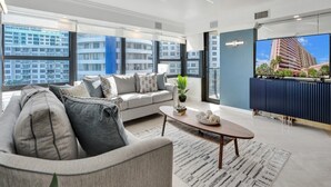 A modern living room with a sofa, coffee table, and a large window offering a city view. - Spacious Ocean View Condo w/ Beach Service, Pool, Gym 803 (Miami Beach)