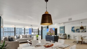 A spacious living area with a dining table, sofas, and a large window offering a city view. - Spacious Ocean View Condo w/ Beach Service, Pool, Gym 803 (Miami Beach)