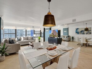 A spacious living area with a dining table, sofas, and a large window offering a city view. - Spacious Ocean View Condo w/ Beach Service, Pool, Gym 803 (Miami Beach)