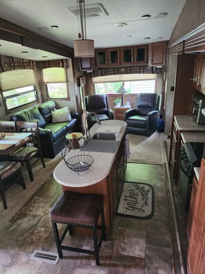 En kompakt autocamper-indretning med et tekøkken, siddeområde og et vindue der giver naturligt lys.