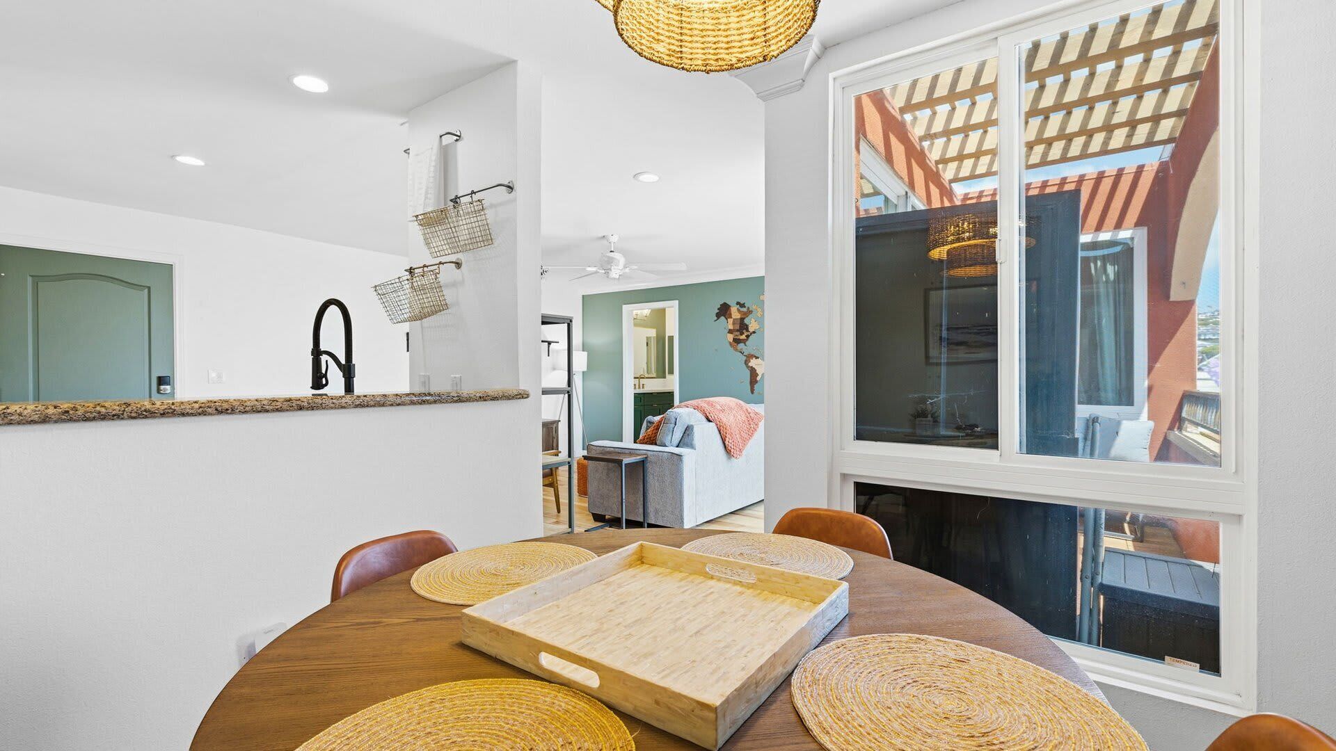 A modern dining area with a round table, woven placemats, and a view of a balcony with a wooden pergola.