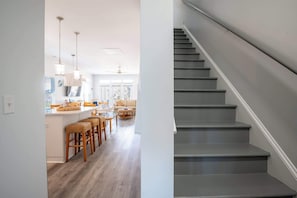 Eine Treppe mit modernem Design, ein Küchenbereich mit hölzernen Barhocker und ein Esstisch.