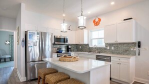 Una cucina moderna con elettrodomestici in acciaio inossidabile, un'isola centrale con sgabelli, mobili bianchi e una parete backsplash rivestita di piastrelle verdi.