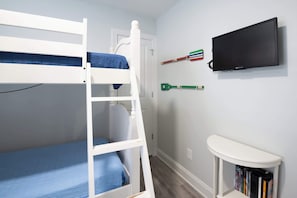 Ein Stockbett, ein Fernseher und ein kleiner Tisch mit Büchern in einem Zimmer mit hellen Wänden.
