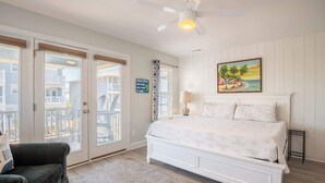 Una camera da letto con un letto bianco, una ventola a soffitto, un quadro e vista sull'esterno.