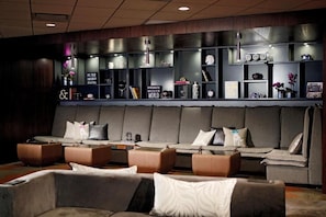 A modern lounge area with a sofa, armchairs, and a wall-mounted shelf with various items.