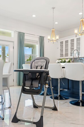 Eine moderne Küche mit Hochstuhl, weißen Stühlen und einer blauen Bar.
