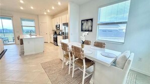 A modern kitchen with white cabinets, a central island, and a dining area with a white table and chairs. - Centrally-located coach home. (Punta Gorda)
