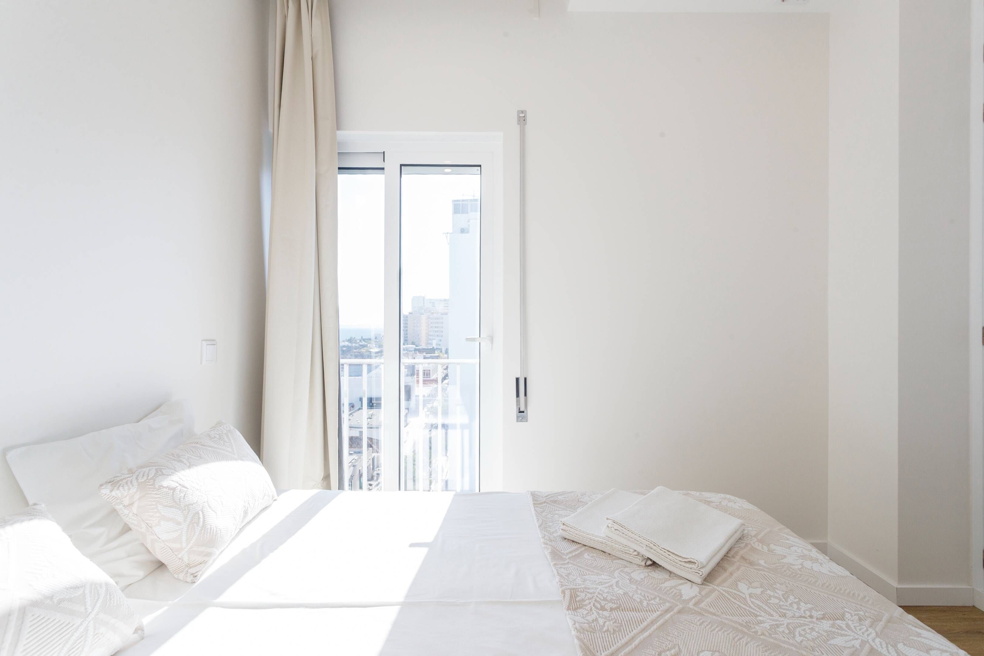 A bedroom with a bed, a window, and a view of buildings.