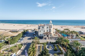 A coastal hotel with a central courtyard, a beach in the background, and a parking area. - Rocha Ocean View Apartment (Portimão)
