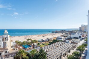 A coastal cityscape with a beach, a swimming pool, and a mix of residential and commercial buildings. - Rocha Ocean View Apartment (Portimão)
