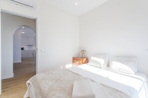 A bedroom with a large bed, a bedside table with a lamp, and a view of a kitchen through an open doorway. - Rocha Ocean View Apartment (Portimão)