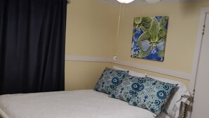 A bedroom with a bed, a ceiling fan, a painting, and a door.
