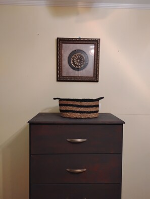 Une commode en bois foncĂ©, dotĂ©e de deux tiroirs et surmontĂ©e dâun panier en osier.