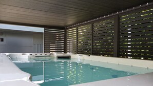 En modern inomhuspool med klart vatten, omgiven av ett träpanelat tak och en vägg med horisontella ribbor.