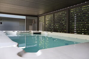 Una piscina interior moderna con agua cristalina, rodeada por un techo de madera y una pared con listones horizontales.
