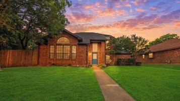 A brick house with a front yard, a wooden fence, and a clear sky.