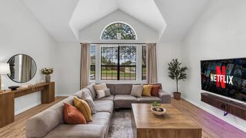 A modern living room with a sectional sofa, a coffee table, a TV, and a large window with curtains.