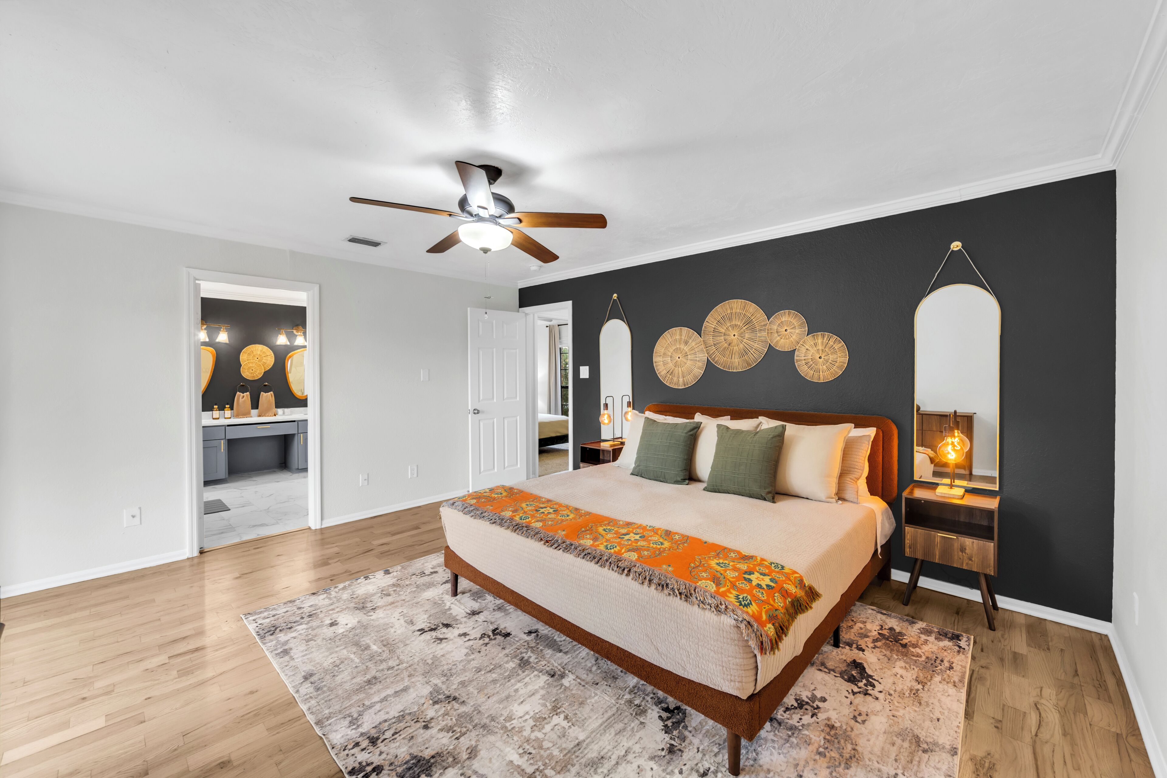 A bedroom with a bed, a ceiling fan, a nightstand, and a wall-mounted mirror.