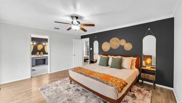 A bedroom with a bed, a ceiling fan, a nightstand, and a wall-mounted mirror.