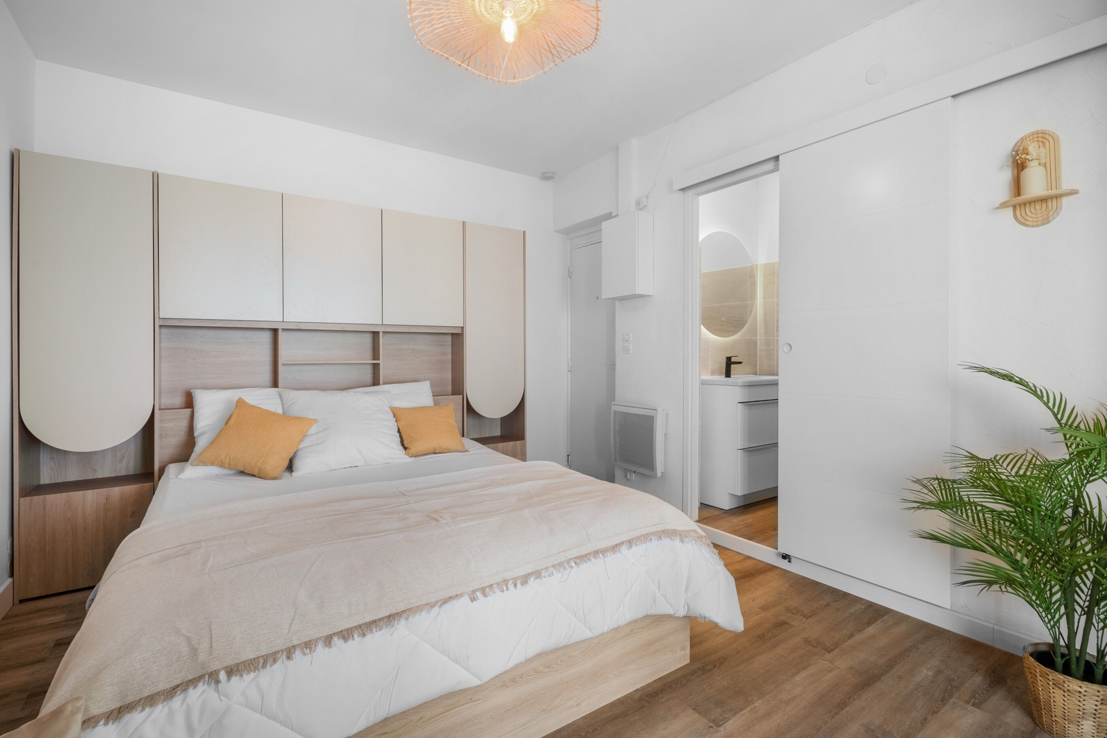 Une chambre moderne avec un grand lit, des rangements intégrés, une table de chevet et une plante en pot.