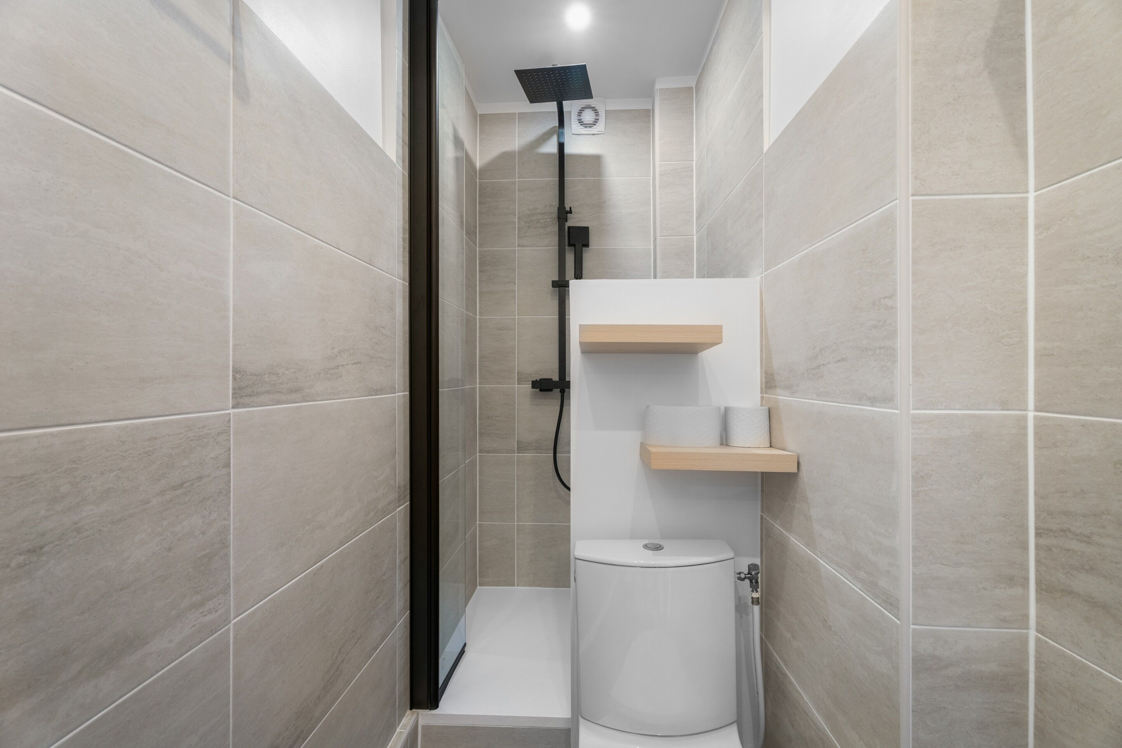 Une salle de bain moderne équipée d’une douche, de toilettes et d’étagères de rangement.