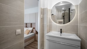 Ein modernes Badezimmer mit rundem Spiegel, Waschbecken und Duschbereich.