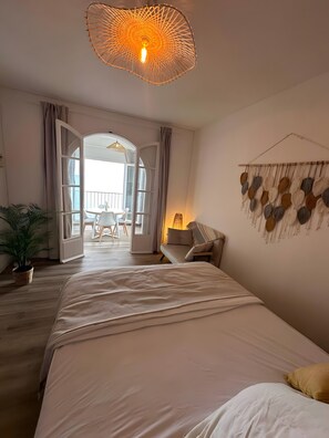 Ein Schlafzimmer mit einem Bett, einer HĂ€ngelampe, einer Wanddekoration und einer offenen TĂŒr, die auf einen Balkon fĂŒhrt.