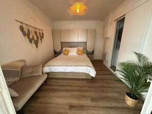 Ein modernes Schlafzimmer mit Bett, Sofa, Wandkunst und einer Zimmerpflanze.