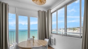 Ein Zimmer mit rundem Tisch, weißen Stühlen, Meerblick und einem Balkon mit Geländer.