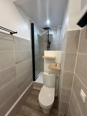 Une petite salle de bain comprenant des toilettes, une douche et un porte-serviettes.