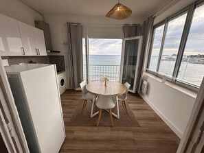 Une cuisine moderne avec des meubles blancs, un coin repas dotĂ© dâune table ronde et de chaises, et une vue sur la mer grĂące Ă de grandes fenĂȘtres.