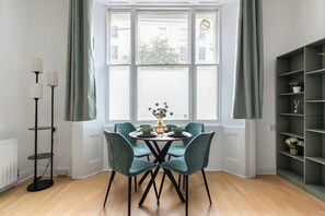 Et spiseområde med et rundt bord, fire stole, en vase med blomster og en reol.