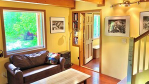 A cozy living room with a sofa, a coffee table, a bookshelf, and framed pictures on the wall. - Beautiful, private  2-bedroom cabin only a few miles from downtown Talkeetna (Talkeetna)