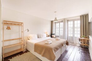 Ein Hotelzimmer mit Bett, einer Holzregaleinheit, einem Schreibtisch mit Stuhl und einem Fenster mit Vorhängen.