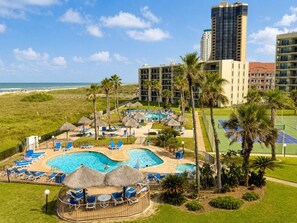 A resort with a swimming pool, lounge chairs, and palm trees. - Oceanfront Condo with Full Kitchen & Pet-Friendly (South Padre Island)