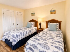 Une chambre avec deux lits simples, une table de chevet avec une lampe et une porte dotée d’un porte-manteau.