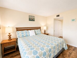 A bedroom with a bed, two bedside tables with lamps, a door, and a wall-mounted picture. - Oceanfront Condo with Full Kitchen & Pet-Friendly (South Padre Island)