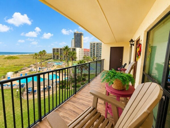 Un balcon donnant sur une piscine et une plage, avec une plante en pot et une chaise.