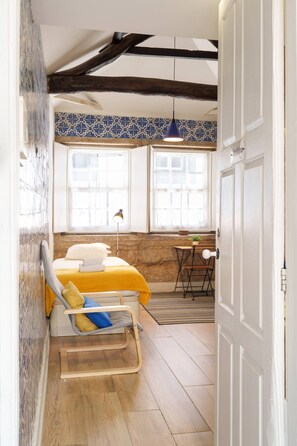 A bedroom with a bed, a chair, a desk, a window, and a hanging light fixture. - VIVA Porto Tile Studios 4T (Porto)