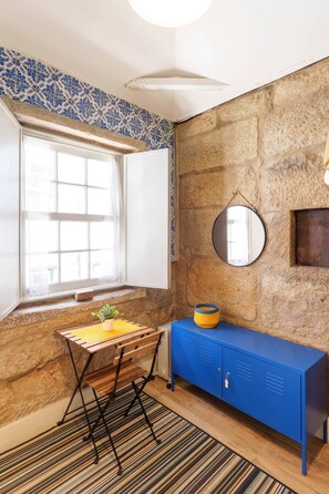 A room with a stone wall, a blue cabinet, a wooden table with a plant, and a window with white curtains. - VIVA Porto Tile Studios 4T (Porto)